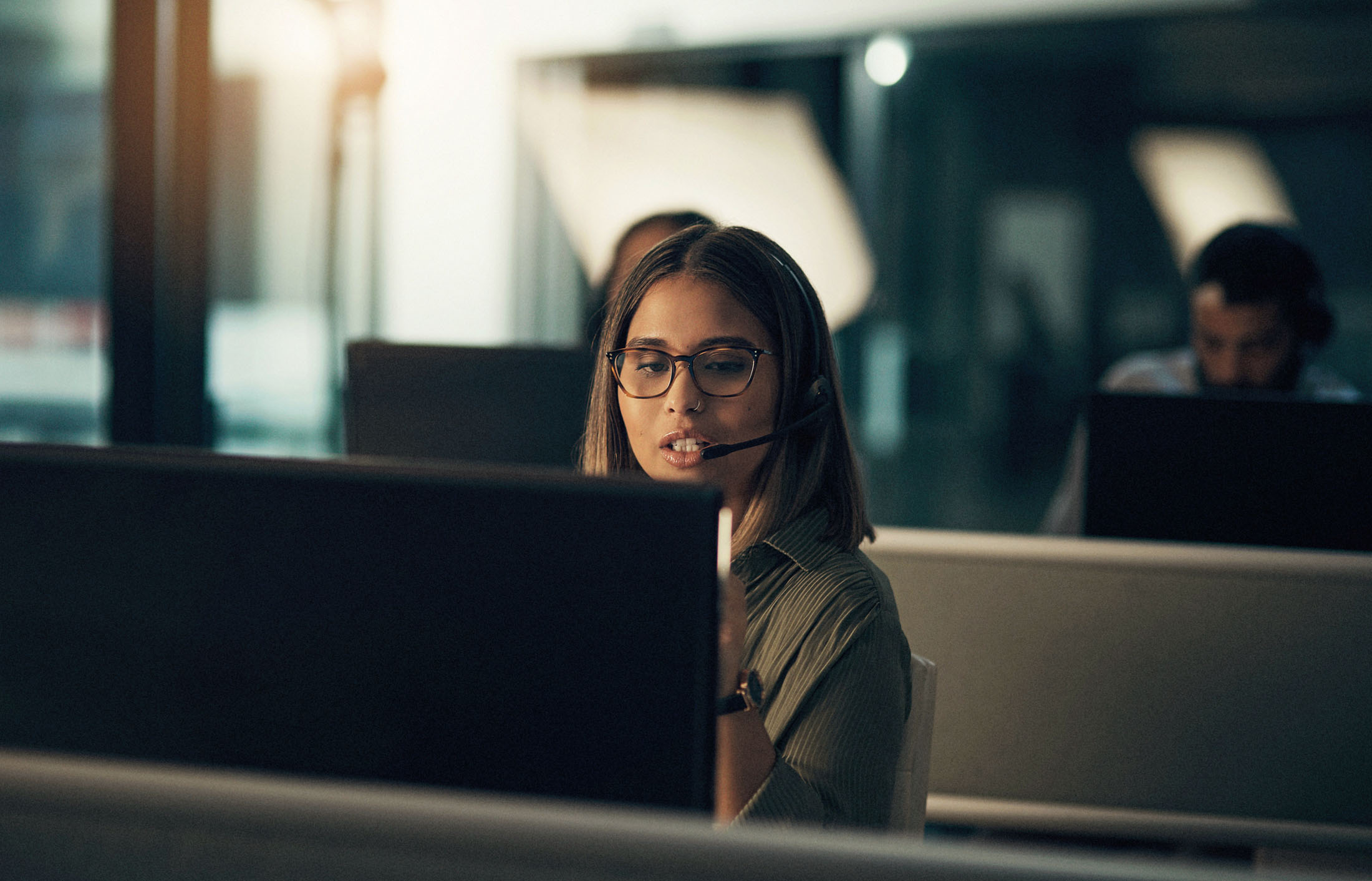 Frau mit Headset und Brille arbeitet konzentriert am Computer.