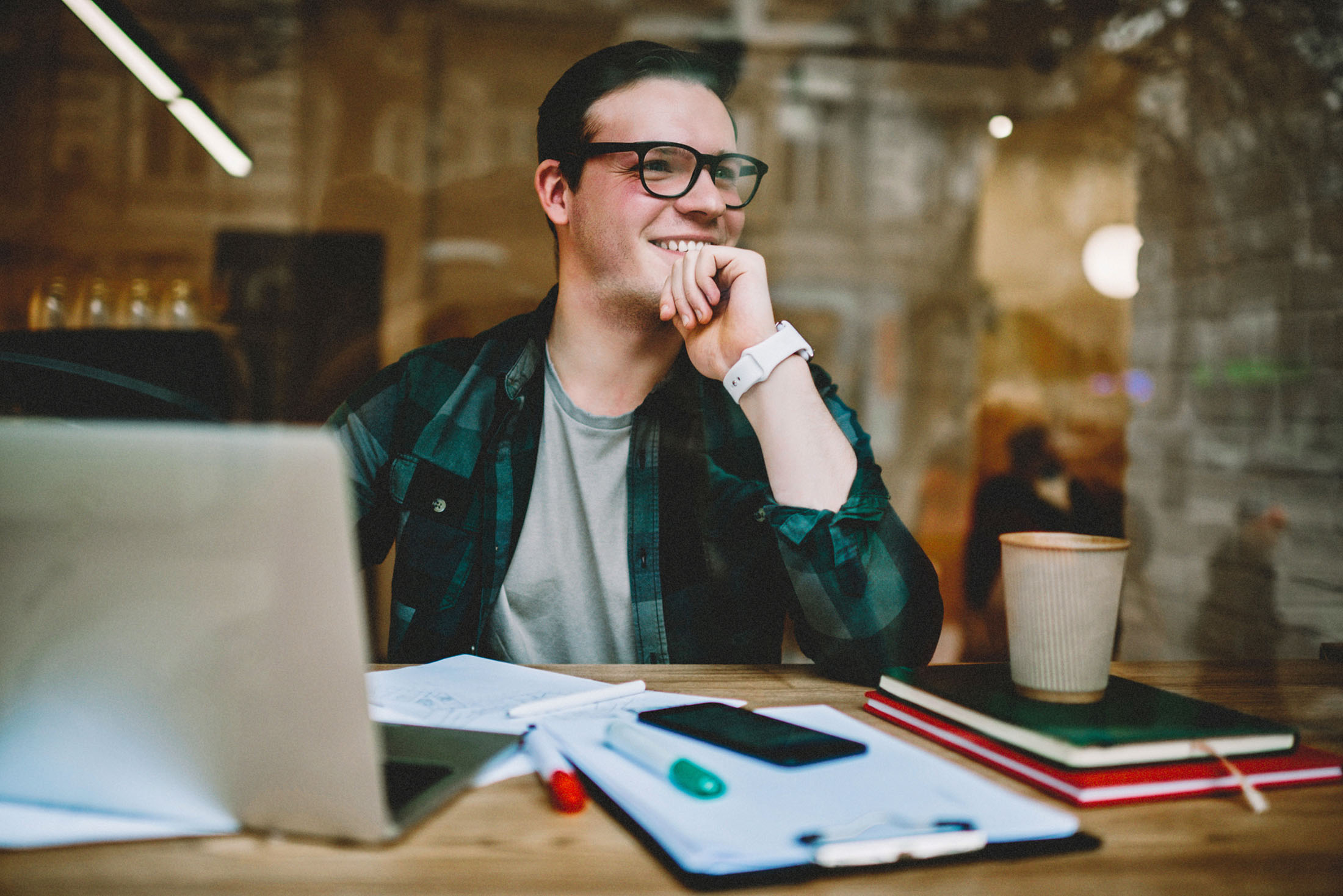 Mann mit Brille sitzt entspannt lächelnd am Laptop in einem Café.